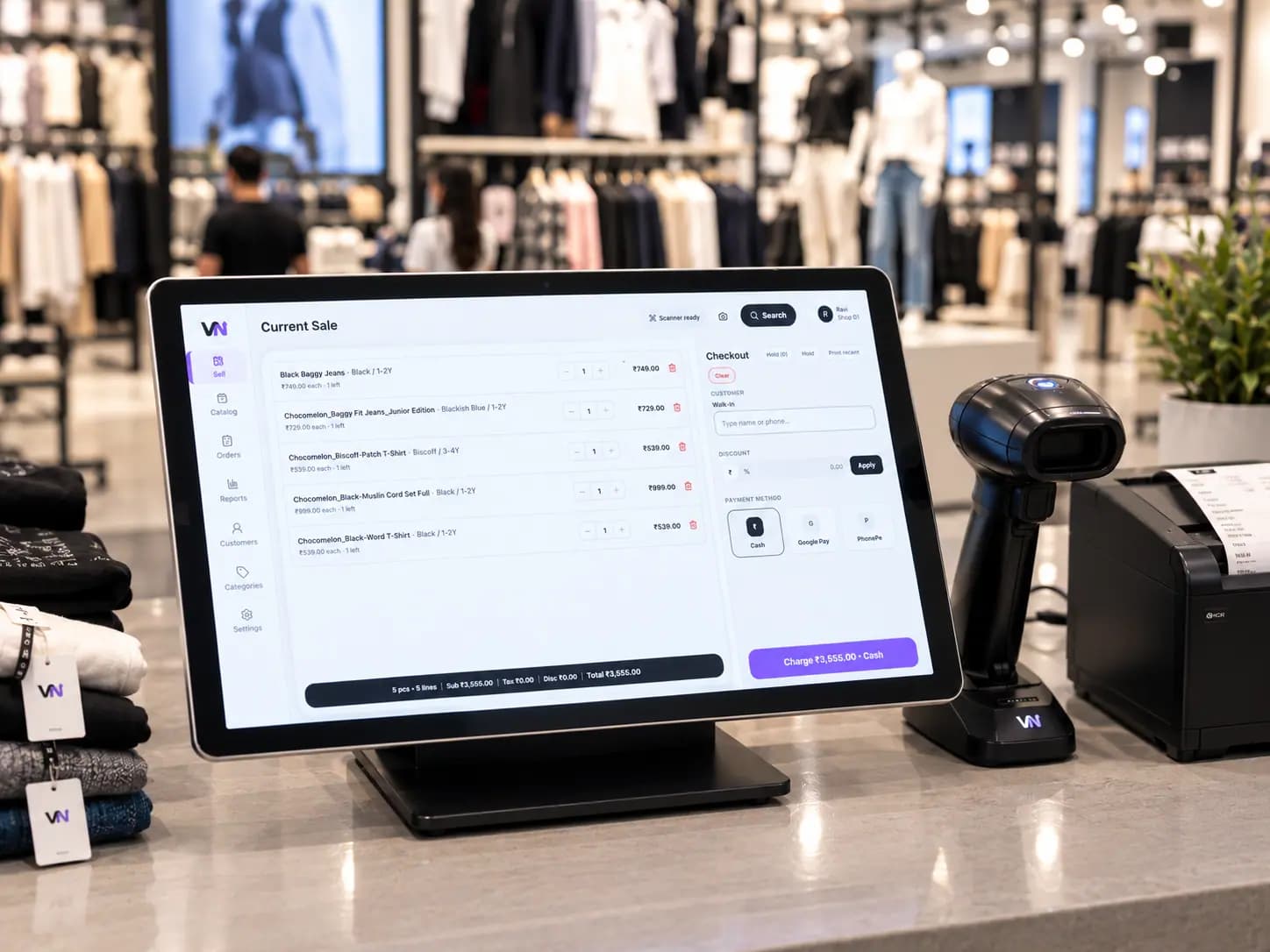 VyaparNext tablet POS with barcode scanner and tagged garments on retail counter